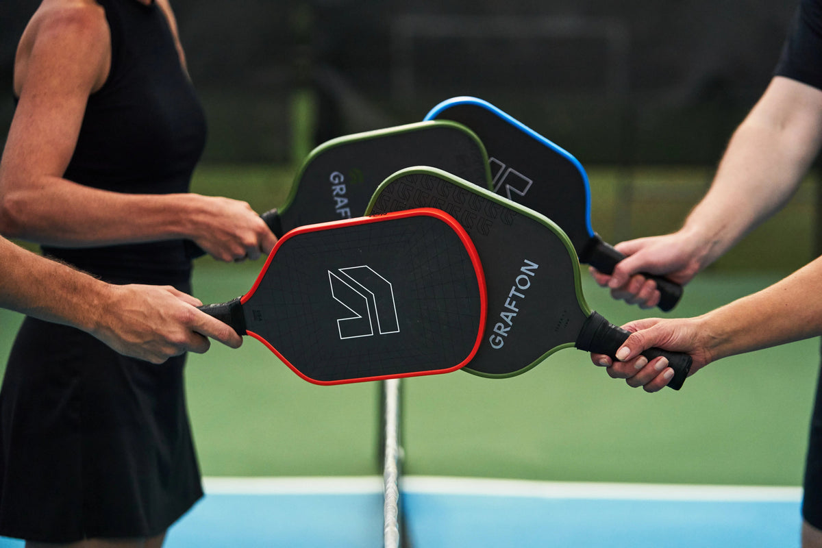 Four people clinking Grafton pickleball paddles together on a court.