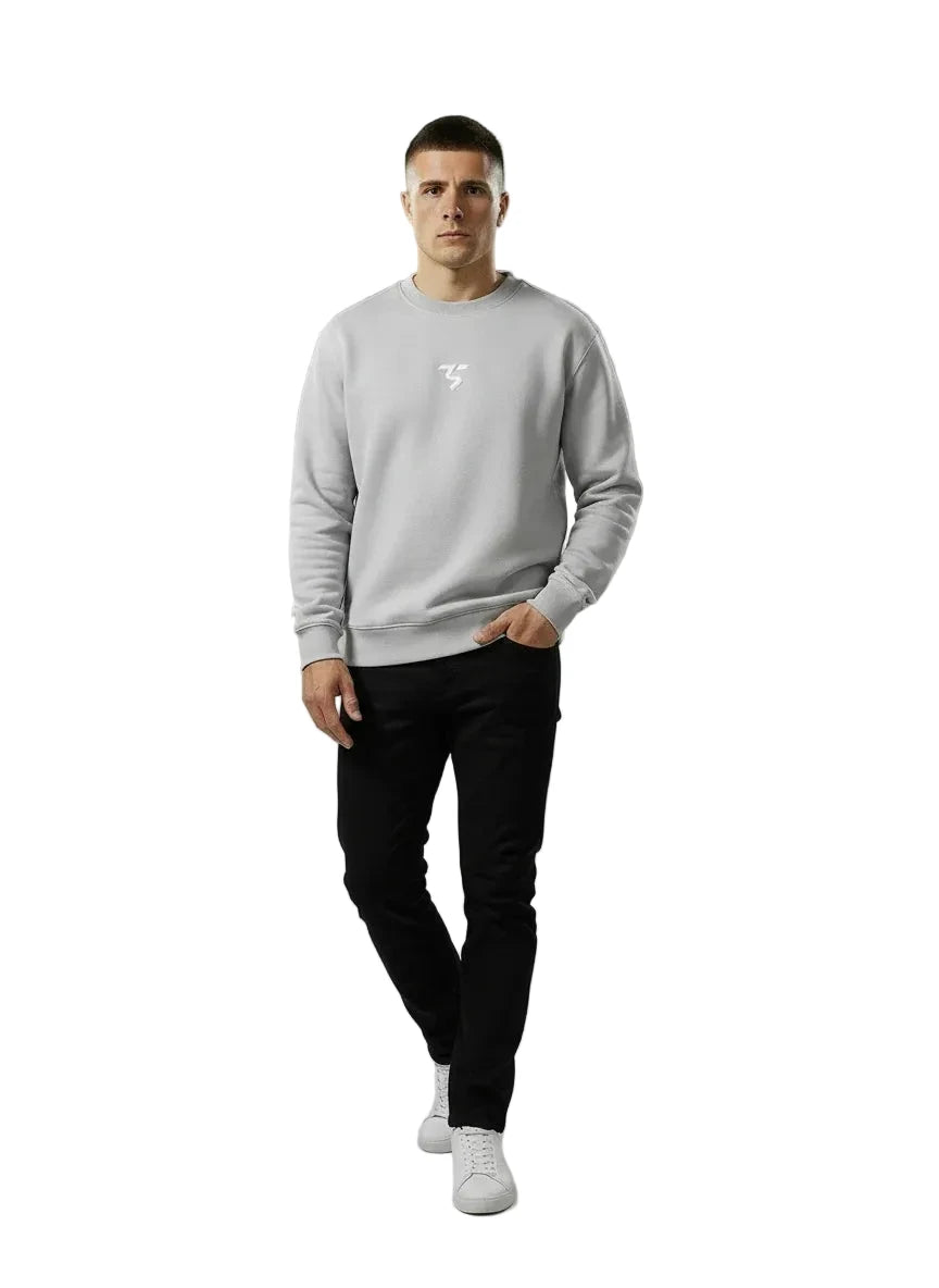 Man wearing a gray sweatshirt with a logo, black pants, and white sneakers on a gray background